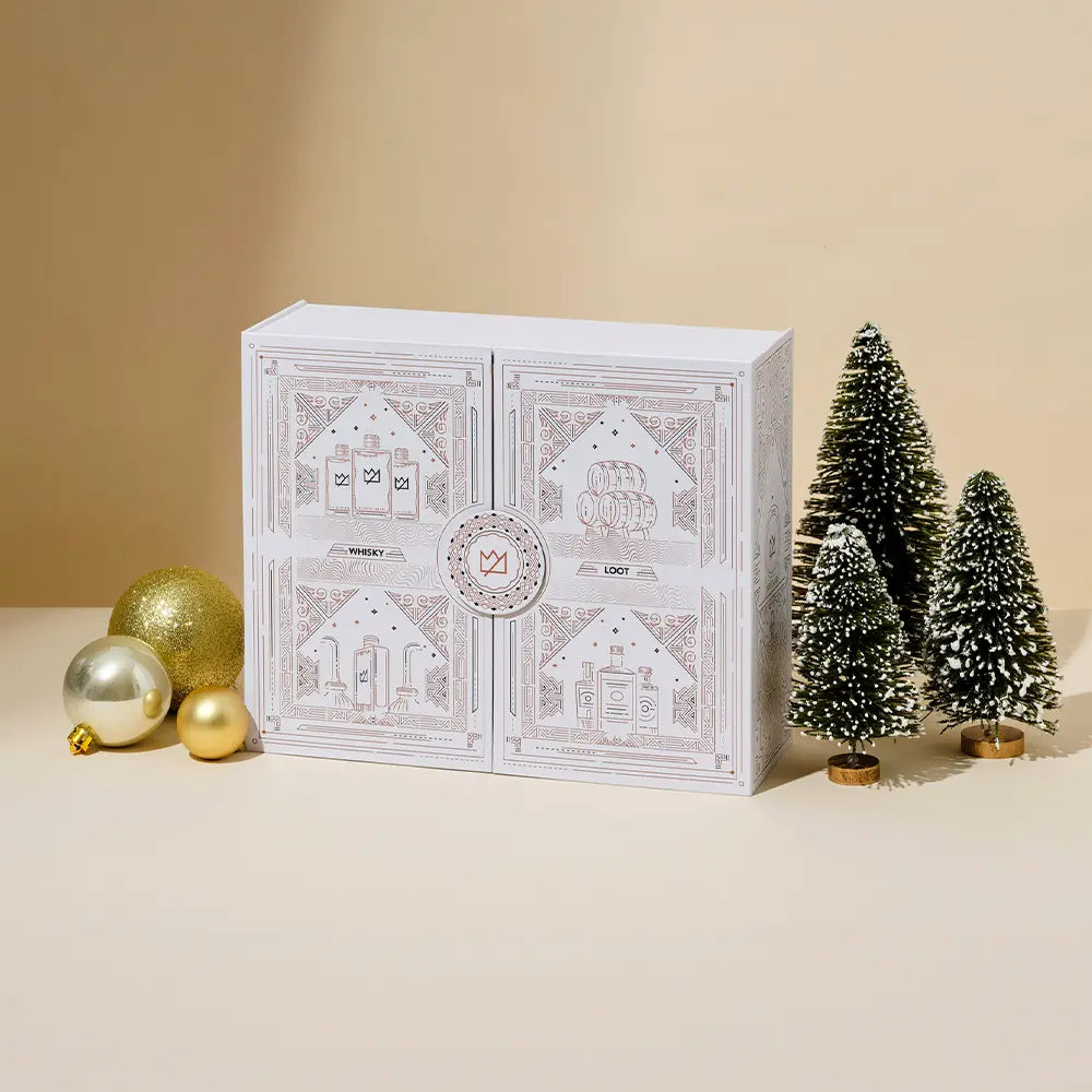 Holiday gift box with decorative trees and golden ornaments nearby.